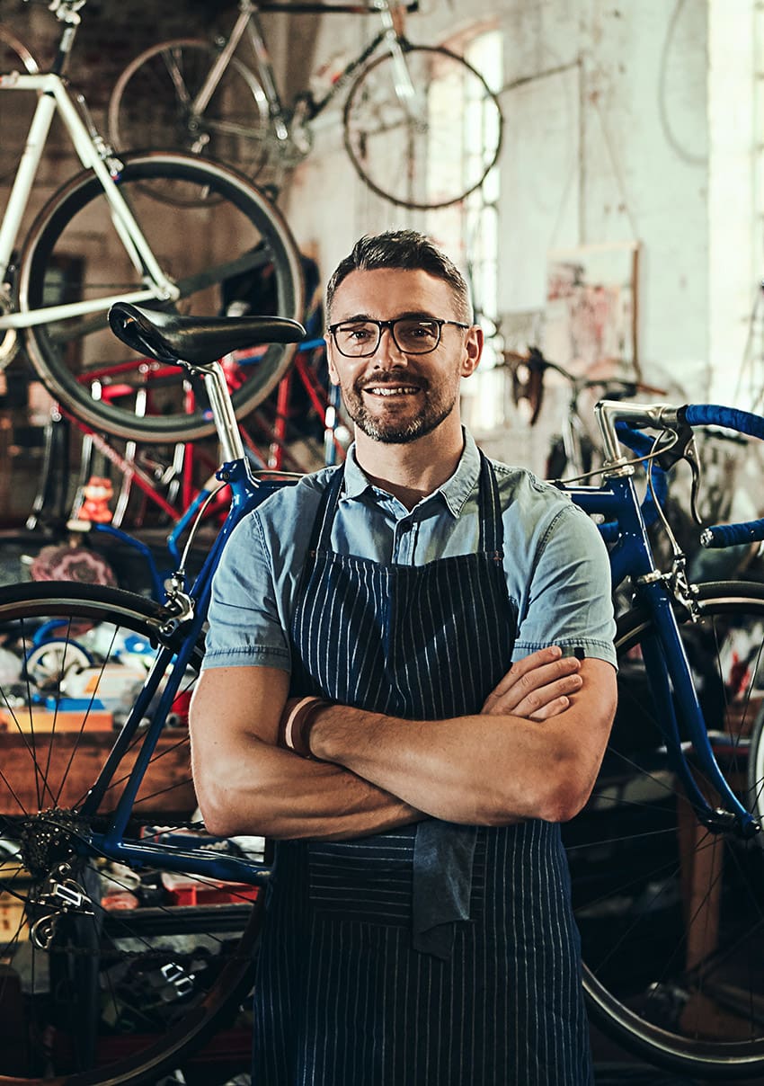 A man in an apron stands outside a bicycle shop.
